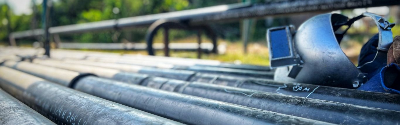 Large industrial pipes with a welding mask sitting on top of the pipes outdoors